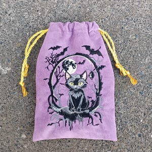 May include: A lavender drawstring pouch featuring an embroidered black cat sitting on a crescent moon. The design includes a full moon, bare tree branches, and flying bats in black thread. The pouch has bright yellow twisted cord drawstrings.