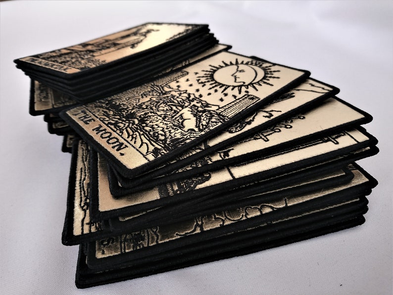 May include: A stack of tarot cards with black borders and cream colored card faces. The top card is The Moon card with a crescent moon and two towers in the background.
