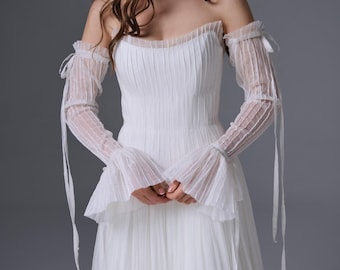 May include: A white floor-length dress featuring a pleated bodice and skirt, paired with matching sheer, pleated, off-the-shoulder long sleeves that have tie-up details at the upper arms and flared cuffs, along with a coordinating sheer neck scarf.