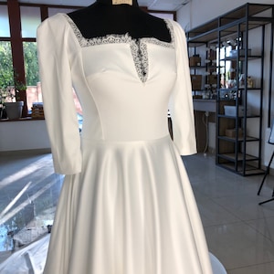 Vestido de novia vintage de satén con escote cuadrado y cola estilo catedral, mangas 3/4 y borde de encaje francés en el escote.
