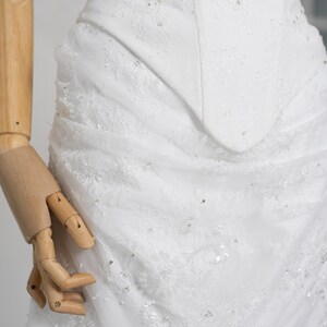 May include: A white wedding dress with intricate lace detailing and sparkling embellishments. The bodice features a fitted design, and the skirt has a layered, textured appearance. The dress is a classic bridal gown.