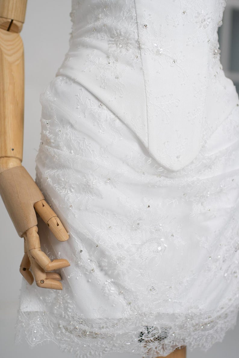 May include: A white wedding dress with intricate lace detailing and sparkling embellishments. The bodice features a fitted design, and the skirt has a layered, textured appearance. The dress is a classic bridal gown.