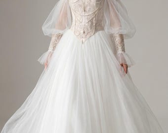 Pode incluir: Um vestido longo com ombros à mostra, apresentando um corpete tipo espartilho bege com bordados intrincados e correntes drapeadas tipo pérola. O vestido inclui mangas bufantes de tule transparente, punhos de renda e uma saia de tule branco.