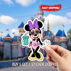 May include: A Minnie Mouse sticker featuring Minnie wearing heart-shaped sunglasses, a purple bow, and a pink dress, holding a teal drink. The sticker has a white border and is set against a blurred background of a castle and blue sky.