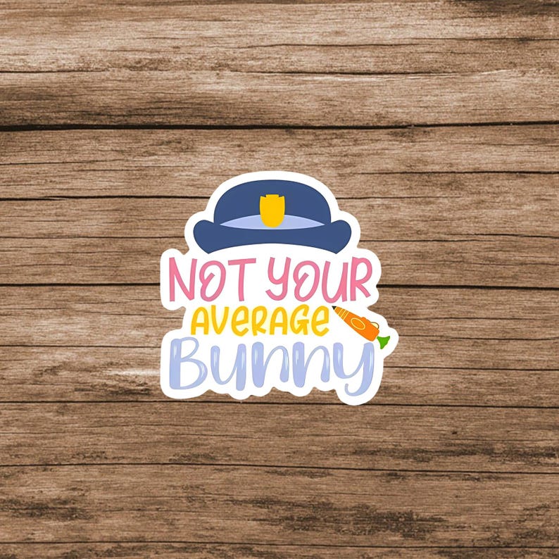 May include: A die-cut sticker featuring a dark blue police hat with a yellow badge on top. Below the hat, the text reads NOT YOUR AVERAGE BUNNY in pink, yellow, and light blue letters. An orange carrot graphic is positioned next to the word AVERAGE.