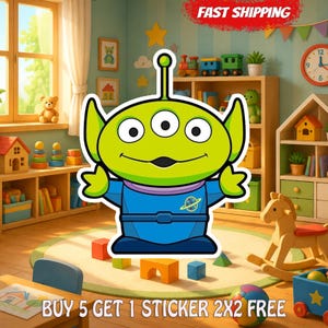 May include: A die-cut sticker featuring a lime green three-eyed alien character with a single antenna, wearing a blue space suit with a yellow planet emblem on the chest. The character has pointed ears and a wide smile, outlined in a thick white border.