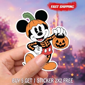 May include: A die-cut vinyl sticker featuring a cartoon mouse character wearing a pumpkin hat and a skeleton-print shirt, holding a small orange jack-o'-lantern bucket. The character has black ears, white gloves, and red shorts with two white buttons.