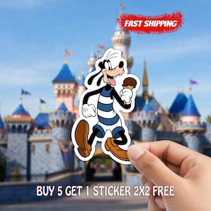 May include: A sticker featuring Goofy in a blue and white striped outfit, holding an ice cream cone. The sticker is held in front of a blurred background of a castle. The text "FAST SHIPPING" is in a red banner. The text "BUY 5 GET 1 STICKER 2X2 FREE" is at the bottom.