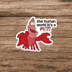 Pode incluir: Um adesivo recortado apresentando um caranguejo vermelho com garras grandes e uma express&atilde;o sorridente. Ao lado do personagem, o texto diz: the human world it's a MESS, com a palavra MESS impressa em fonte vermelha negrito sobre fundo branco.