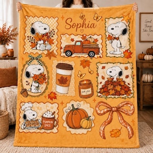 May include: A soft orange fleece blanket featuring Snoopy in various autumn scenes, including holding leaves, sitting in a pile of leaves, and baking. The design includes a truck, a pumpkin, a coffee cup, a bow, and the name Sophia in script.
