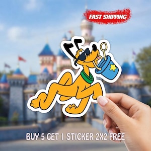 May include: A yellow Pluto sticker with black sunglasses, a green collar, and a blue bucket with a yellow star. The sticker is held by a hand in front of a blurred castle background. Text reads "FAST SHIPPING" and "BUY 5 GET 1 STICKER 2X2 FREE".