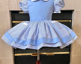Puede incluir: Un vestido a rayas azules y blancas con cuello blanco y mangas abullonadas. El vestido tiene una diadema azul con lazo.