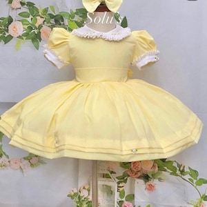 May include: A yellow dress with a white lace collar and puffed sleeves. The dress has a full skirt and is decorated with small white flowers.