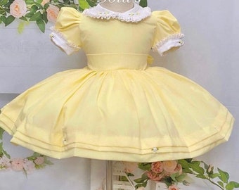 May include: A yellow dress with a white lace collar and puffed sleeves. The dress has a full skirt and is decorated with small white flowers.