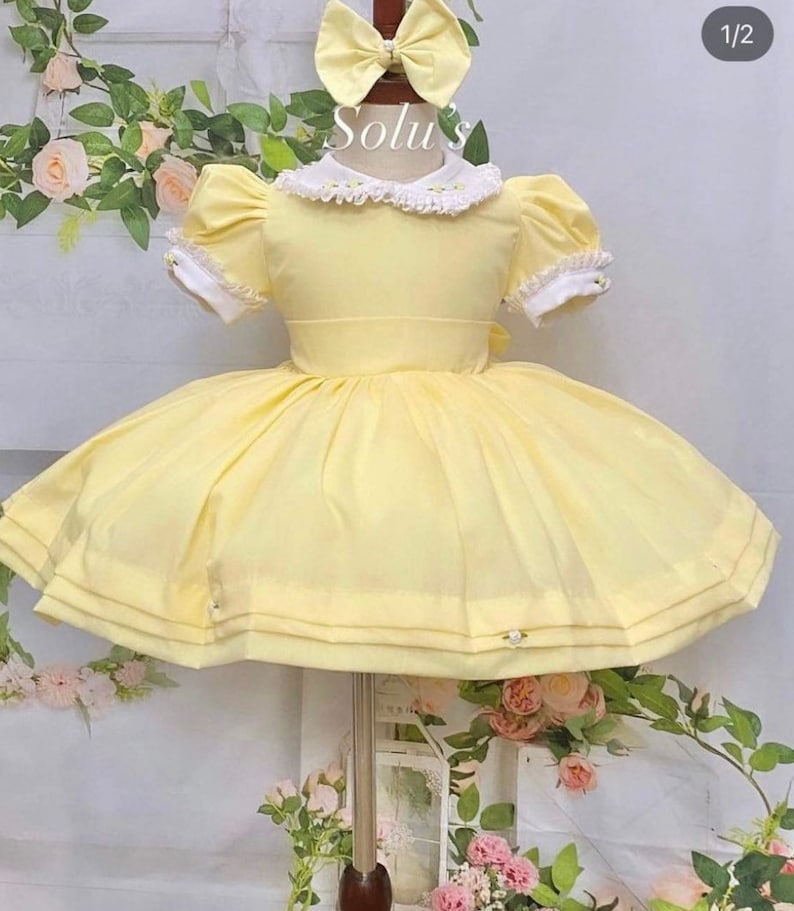 May include: A yellow dress with a white lace collar and puffed sleeves. The dress has a full skirt and is decorated with small white flowers.