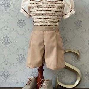 May include: A brown and white striped knitted top with a white Peter Pan collar and puffed sleeves. The top is paired with beige shorts and silver leather shoes.