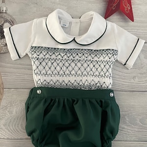 May include: A white and green baby outfit with a peter pan collar and short sleeves. The outfit has a smocked bodice and a green nappy cover.
