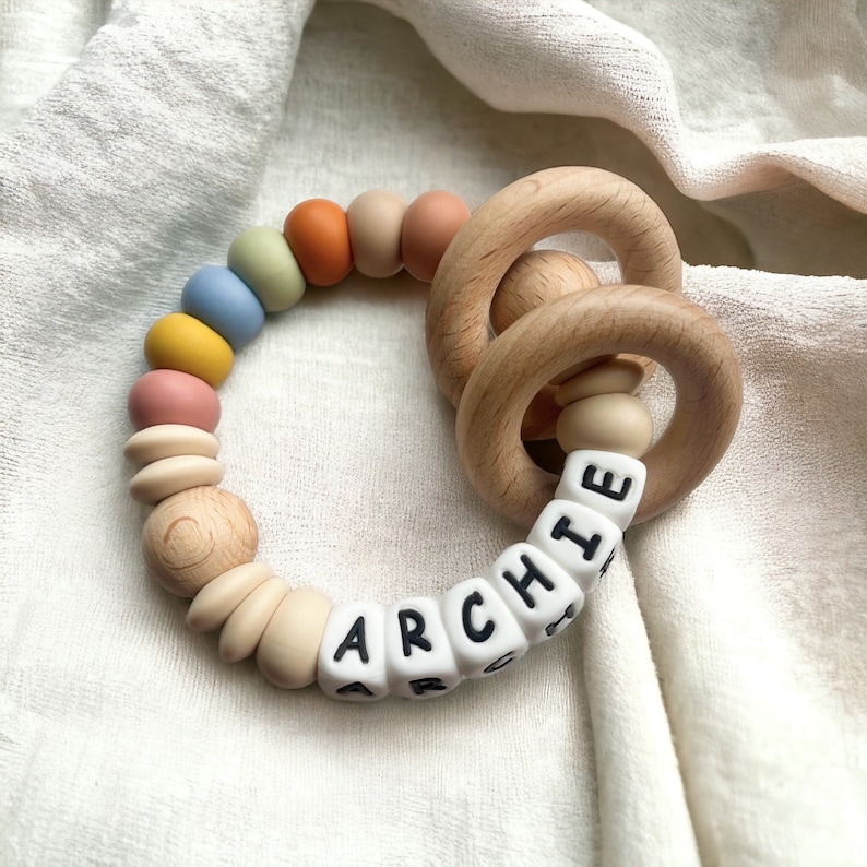 May include: A wooden teething ring with a colorful silicone bead chain and white letter beads spelling "ARCHIE".