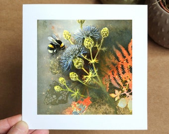 May include: A watercolor painting of a bee flying near a cluster of blue and yellow flowers with a fern in the background.