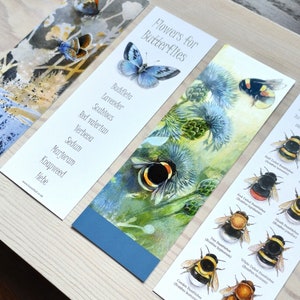 May include: Three bookmarks with watercolor illustrations of flowers and bees. The first bookmark lists flowers that attract butterflies, the second bookmark shows a bee on a thistle flower, and the third bookmark shows a guide to identifying British bumblebees.