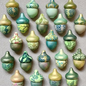 Könnte beinhalten: Eine Sammlung von 20 handbemalten Eichel-Ornamenten in verschiedenen Grüntönen, Blau- und Goldtönen. Jede Eichel hat ein einzigartiges Design und aufwendige Details.