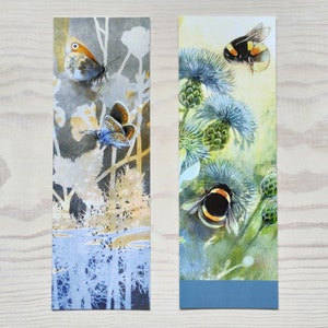 May include: Two watercolor bookmarks featuring nature scenes. The first bookmark shows a blue butterfly and a brown butterfly on a white and gray background. The second bookmark shows a bumblebee and a yellow and black bumblebee on a green and blue background.