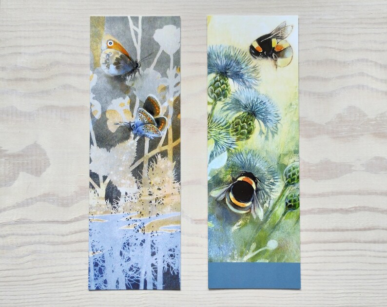 May include: Two watercolor bookmarks featuring nature scenes. The first bookmark shows a blue butterfly and a brown butterfly on a white and gray background. The second bookmark shows a bumblebee and a yellow and black bumblebee on a green and blue background.