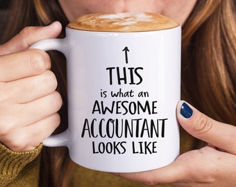 May include: White coffee mug with black text that reads "This is what an awesome accountant looks like" with an arrow pointing up.