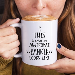 May include: White coffee mug with black text that reads "This is what an awesome >>Banker<< looks like".