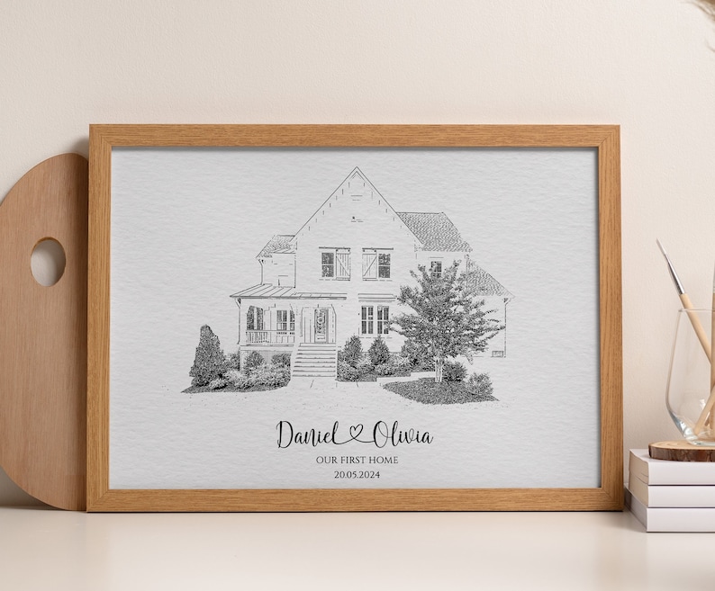 Pode incluir: Um desenho a preto e branco de uma casa com uma varanda da frente e uma &aacute;rvore no quintal. O desenho est&aacute; emoldurado numa moldura de madeira castanho claro. O texto "Daniel & Olivia Our First Home 2005 2024" est&aacute; impresso abaixo do desenho.