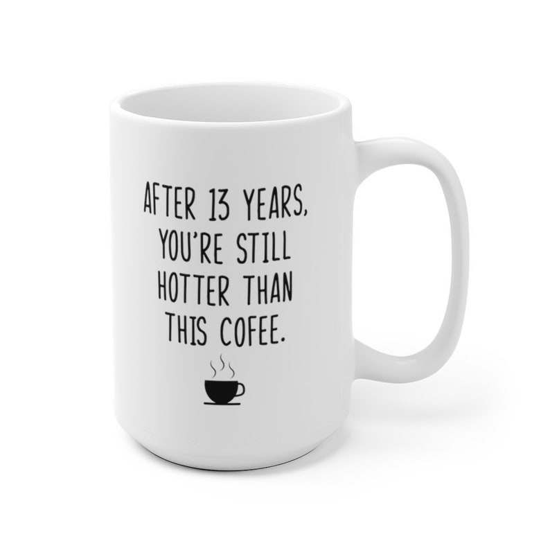 May include: White ceramic coffee mug with black text that reads "After 13 years, you're still hotter than this coffee." A small black and white illustration of a coffee cup with steam coming from it is below the text.