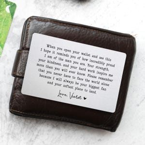 May include: A brown leather wallet with a white card insert. The card has a printed message in black text, including the words "Love, Violet" and a heart symbol. The wallet is closed.