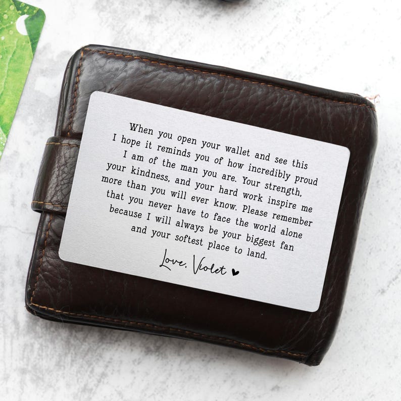 May include: A brown leather wallet with a white card insert. The card has a printed message in black text, including the words "Love, Violet" and a heart symbol. The wallet is closed.