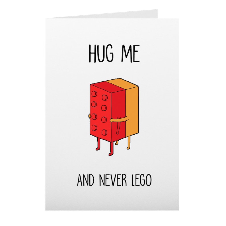 May include: A white greeting card with the words "HUG ME" at the top and "AND NEVER LEGO" at the bottom. The card features a cartoon illustration of two Lego bricks hugging. One brick is red, the other is orange.