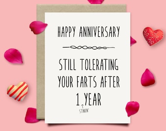 May include: A white card with black text that reads "Happy Anniversary - Still Tolerating Your Farts After 1 Year - Stinkin'". The card is surrounded by pink rose petals and red hearts.