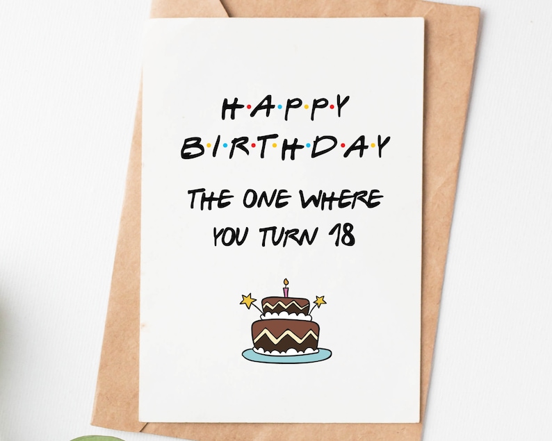 May include: A white card with black text that reads "Happy Birthday The One Where You Turn 18". The card has a cartoon image of a chocolate cake with a single lit candle and sprinkles.