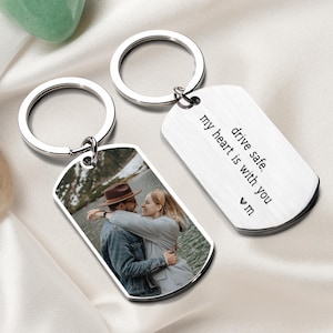 May include: Silver keychain with a photo of a couple hugging and a silver tag with the text "drive safe. my heart is with you ♥ m"