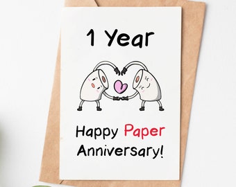 May include: A white card with a black and white illustration of two toilet paper rolls holding hands and forming a heart shape with their arms. The text "1 year" is at the top of the card and the text "Happy Paper Anniversary!" is at the bottom of the card.