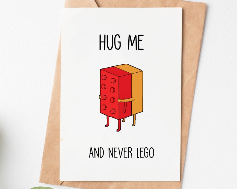May include: A white greeting card with the words "HUG ME AND NEVER LEGO" in black text. The card features a cartoon illustration of a red and yellow Lego brick hugging another Lego brick. The card is inside a brown envelope.