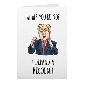 May include: A white greeting card with the text "WHAT? YOU'RE 90? I DEMAND A RECOUNT!" features a cartoon illustration of a man in a suit with blonde hair, red tie, and an angry expression. The card is folded.