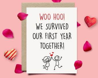 May include: A white card with the text "Woo Hoo! We survived our first year together!" in black lettering.  The card features a simple line drawing of a couple holding hands and jumping for joy.  There are small red hearts above the couple.