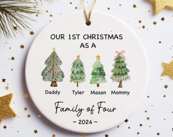 Może przedstawiać: Okrągła, biała ceramiczna ozdoba choinkowa ze złotym sznurkiem. Ozdoba przedstawia cztery ilustrowane choinki i napis "OUR 1ST CHRISTMAS AS A Family of Four ~ 2024~". Pod drzewkami znajdują się imiona Daddy, Tyler, Mason i Mommy.
