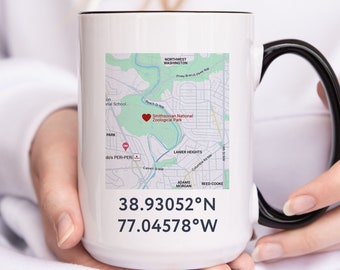 Puede incluir: Taza de cerámica blanca con asa negra. La taza presenta un mapa de Washington, D.C. con un corazón rojo que marca la ubicación del Smithsonian National Zoological Park. La taza también incluye las coordenadas 38.93052°N 77.04578°W.