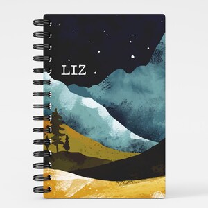 May include: A spiral bound notebook with a watercolor design of mountains, a night sky with stars, and the name "Liz" printed on the front cover.