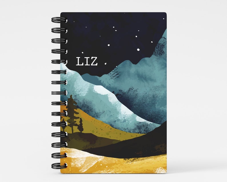 May include: A spiral bound notebook with a watercolor design of mountains, a night sky with stars, and the name "Liz" printed on the front cover.