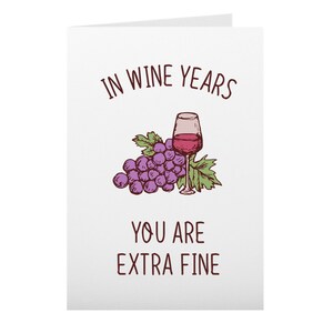 May include: A white card with the text "In wine years you are extra fine" in brown lettering. A cartoon illustration of a bunch of purple grapes and a glass of red wine is above the text.