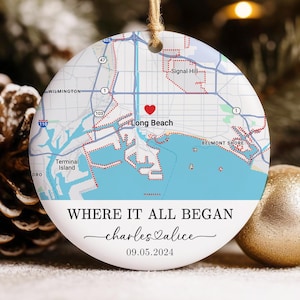 May include: A white ceramic ornament with a map of Long Beach, California, featuring a red heart marking a location. The text "WHERE IT ALL BEGAN" is above the names "charles & alice" and the date "09.05.2024". A jute string is attached for hanging.