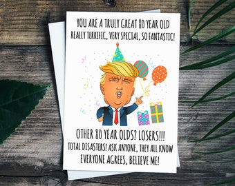 May include: A humorous birthday card featuring a cartoon illustration of Donald Trump wearing a party hat and holding a gift box. The card reads "You are a truly great 80 year old really terrific, very special, so fantastic! Other 80 year olds? Losers!!! Total disasters! Ask anyone, they all know everyone agrees, believe me!"