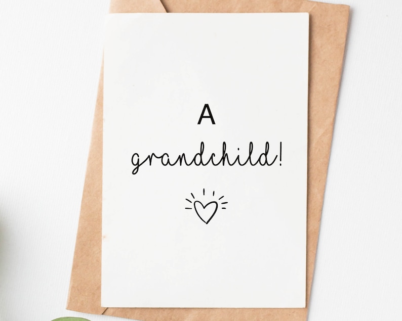 May include: A white card with black text that reads "A grandchild!" with a small heart and radiating lines above it.