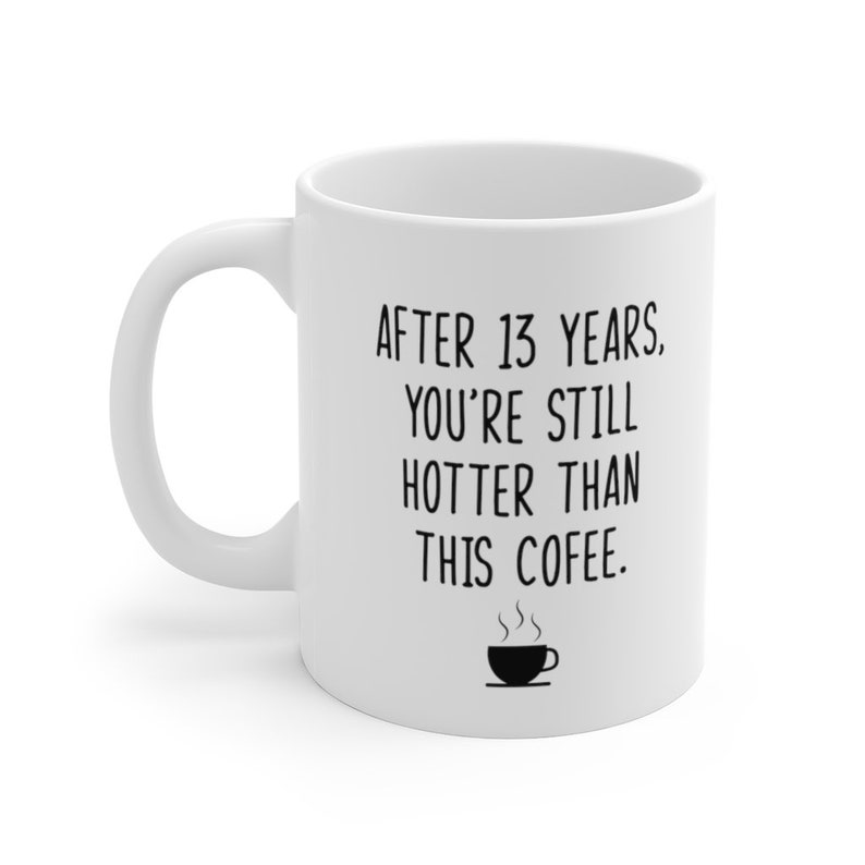 May include: White ceramic coffee mug with black text that reads "After 13 years, you're still hotter than this coffee."  A small black and white illustration of a coffee cup with steam rising from it is below the text.